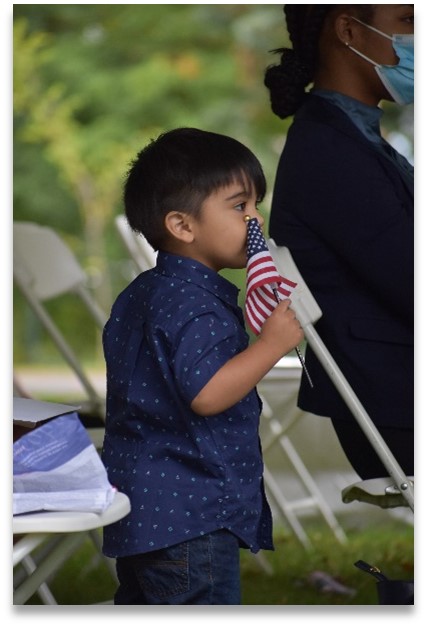 Child holding small American flag at among white folding chairs at a ceremony