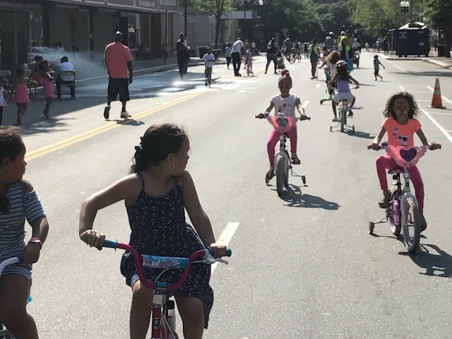 Children riding bicycles with training wheels down a street on a sunny day